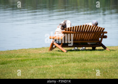 A man and woman sitting on a park bench at Osborne Point on Lake Pleasant in Speculator, NY USA reading the newspaper. Stock Photo