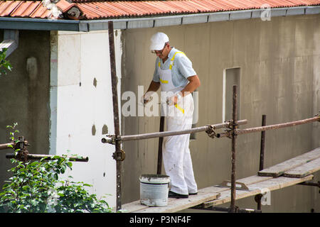 Nis, Serbia - June 16, 2018: Worker man with white uniform is on scaffold. Plasterer insulates new facade wall on house Stock Photo