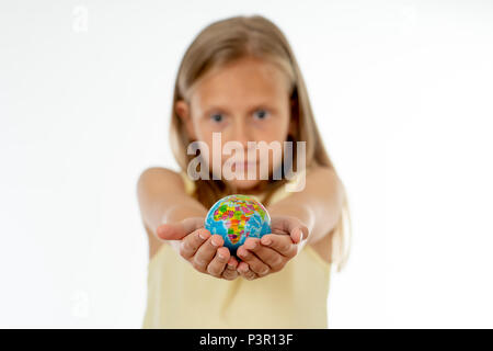 Charming cute little girl out of focus holding a globe, looking at camera and smiling, standing on white background in world learning concept. Stock Photo