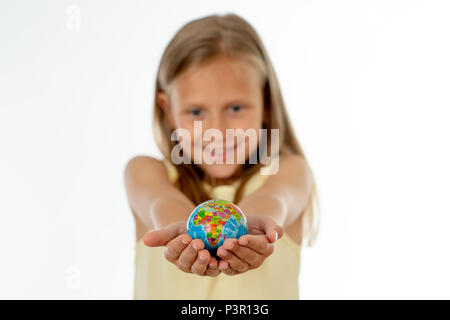 Charming cute little girl out of focus holding a globe, looking at camera and smiling, standing on white background in world learning concept. Stock Photo