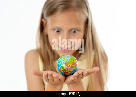 Charming cute little girl out of focus holding a globe, looking at camera and smiling, standing on white background in world learning concept. Stock Photo