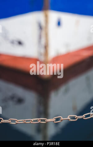 Small protective chain on the edge of a landing in a marina with a water reflection of a small empty fisherman boat in the background Stock Photo