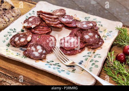 Italian flavors: sliced salami in a plate placed on a wooden table decorated with oregano and cherries - selective focus Stock Photo
