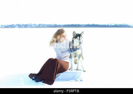 Woman wearing mittens sitting with husky in white snow background. Stock Photo