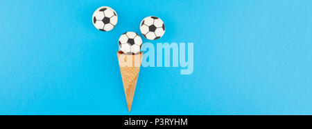 Long wide banner top view of ice cream waffle cones with soccer balls macarons on bright bold blue background with copy space in minimal style, concep Stock Photo