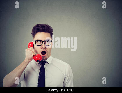 Amazed shocked young business man talking on a red telephone Stock Photo