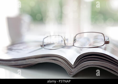 Magazines on a desk with reading glasses Stock Photo