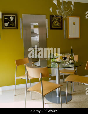 Modern chrome and plywood chairs with circular glass and chrome table in modern yellow dining room Stock Photo