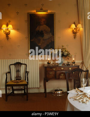 Wall-lights on either side of large oil painting above antique chair and console table in French country dining room Stock Photo