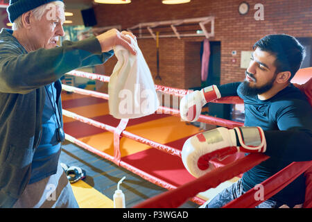 Trainer refreshing boxer on ring Stock Photo