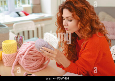 Red-haired needlewoman looking at nice light purple thread Stock Photo