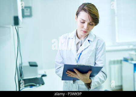 Doctor standing with clipboard and taking notes Stock Photo