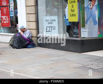 A man, seemingly homeless, sits on the ground outside a shop in Buxton,  High Peak,  Derbyshire,  UK Stock Photo