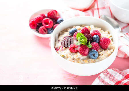 Healthy breakfast. Oatmeal porridge with milk and berries on pink. Stock Photo