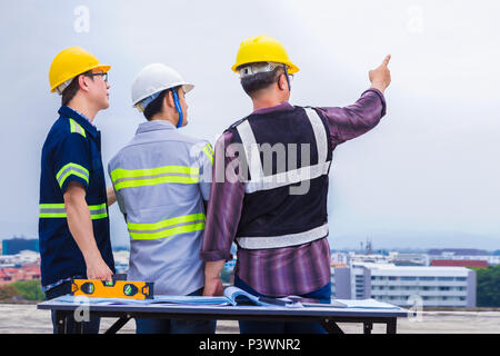 Back side of Asian construction engineer and his foremen working together and pointing at construction site, good for teamwork and engineering theme Stock Photo