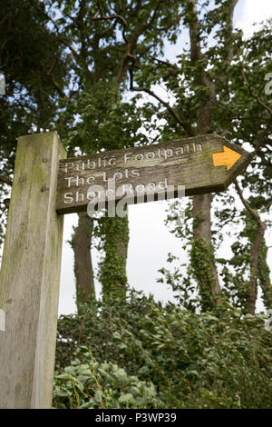A wooden sign close to the seashore indicating a public footpath in the direction to The Lots and Shore Road near Silverdale in Lancashire UK GB Stock Photo