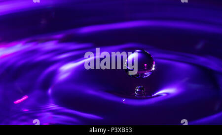 Water drop falling into water making ripples in blue and purple color Stock Photo