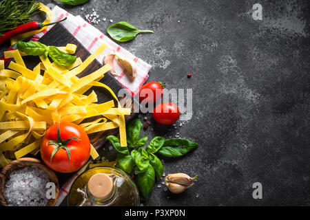 Italian food background. Pasta, tomatoes, basil and olive oil on black stone table. Top view, Copy space. Stock Photo