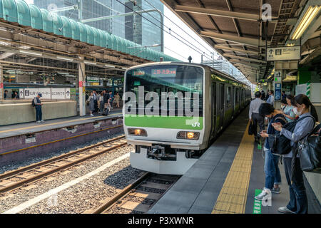 TOKYO, JAPAN 22/05/2018: Train arriving at the trains station while people are waiting and looking at their smartphones Stock Photo