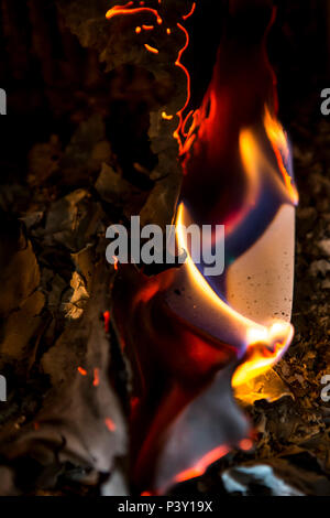 Sheets of white paper burning in a fire grate with small flames, smoke and charred edges. Stock Photo