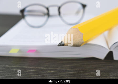 Close up of hipster glasses for reading on an open book with big yellow pencil in office, Shallow Depth of Field and selective focus. Workbook and hom Stock Photo