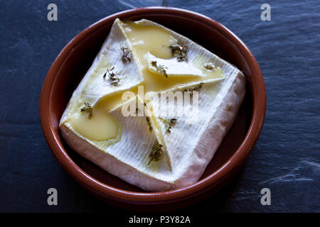 Baked Soft Cheese in a brown ceramic dish Stock Photo