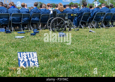 High school graduation mortarboard caps, one lettered with 'LISTEN TO THE KIDS', lie on the ground after being tossed into the air. Stock Photo