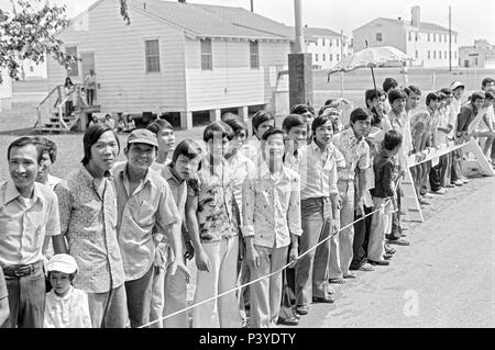 FORT SMITH, AR, USA - AUGUST 10, 1975 -- A line of newly-arrived Vietnamese refugees stand and wait for the passing of President Gerald Ford.  The president is to be touring the Fort Chaffee Vietnamese refugee center and welcoming the evacuated South Vietnamese to the United States.  Behind the people stands rows of the barracks buildings that housed the refugees. Stock Photo