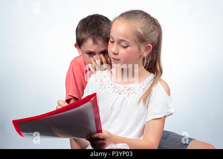 Caucasian schoolchildren studying, a nice girl holding notes, explains a boy who does not understand the subject and holds his hand against his mouth. Stock Photo