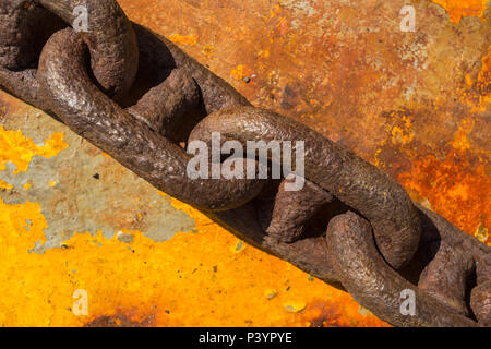 Close-up detail of heavy rusty metal chain links on flat steel plate with peeling yellow paint on Kamenari-Lepetane ferry, Bay of Kotor, Montenegro. Stock Photo