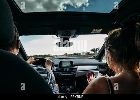 Older couple on front seat of car. Road trip concept. Woman uses a smartphone to pass the time while man drives Stock Photo