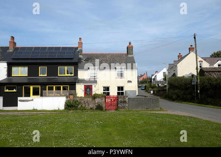 Modern house with solar panels panel and traditional cottage with red gate  in the village of Marloes in Pembrokeshire West Wales, UK  KATHY DEWITT Stock Photo