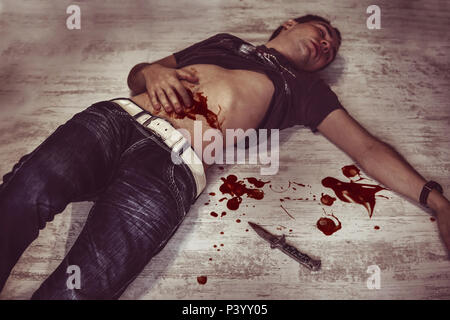 body of a man lying on the floor in a puddle of blood next to the murder weapon, a small folding knife. young man's body on the floor with bloody woun Stock Photo