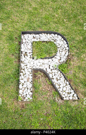 Letter R built from white stones on green grass as seen from high above Stock Photo