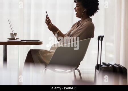 Businesswoman waiting at airport lounge for flight and making video call from her mobile phone. Smiling african female executive at airport waiting ar Stock Photo