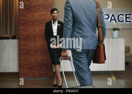 Businessman carrying suitcase and walking towards a receptionist waiting for welcome the guests. Business traveler arriving at hotel for conference. Stock Photo
