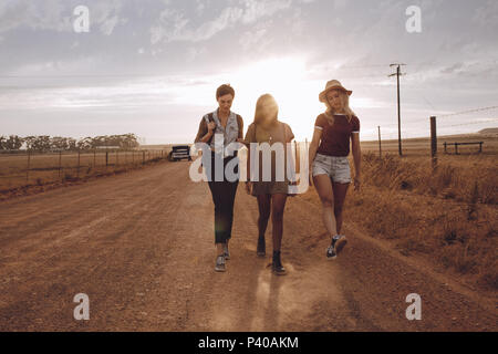 Full length of three disappointed women walking through country road leaving their broken down car behind. Friends leaving broken down car behind on c Stock Photo