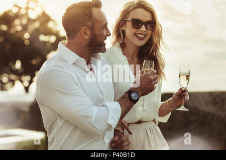 Smiling man and woman enjoying a glass of wine outdoors. Happy couple with a glass of wine sitting outdoors. Stock Photo