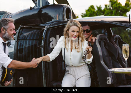 Beautiful young woman disembarking a helicopter with pilot supporting her. Gorgeous young women travelling a helicopter. Stock Photo