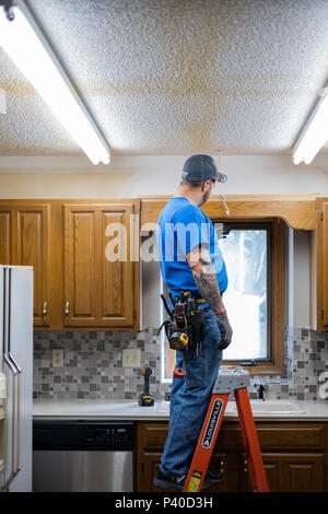 Caucasian man electrician standing on ladder and changing out lights during a kitchen remodel in Wichita, Kansas, USA. Stock Photo