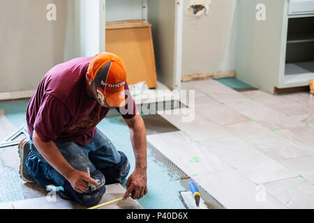 A 40 year old Caucasian man measuring and laying ceramic tile in a home remodel job in Wichita, Kansas, USA. Stock Photo