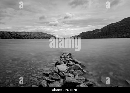 A black and white landscape view of a lake with a collection of rocks leading in to the water. Stock Photo