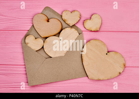 Brown envelope and collection of plywood hearts. Opened envelope from craft paper and wooden hearts for decoupage, top view. Stock Photo