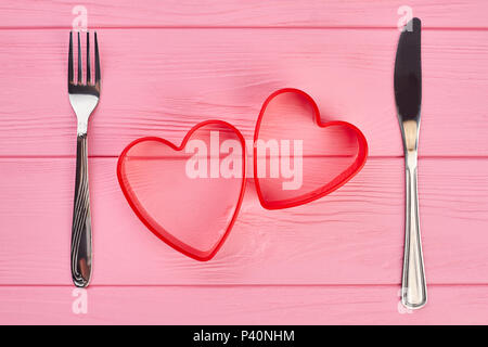 Two red hearts, fork and knife. Table setting with heart shaped cake molds and cutlery. Valentines Day background. Stock Photo