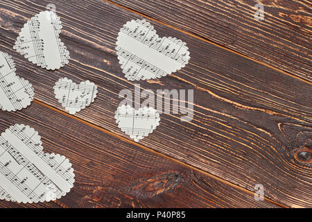 Paper hearts with musical notes on wood. Paper heart shaped figures with music notes on brown wooden background with copy space. Stock Photo