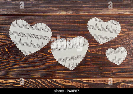 Four paper hearts on wooden background. White paper hearts with musical notes on brown wooden background. Stock Photo