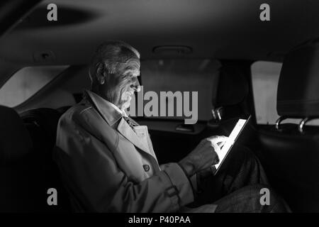 Businessman with a digital tablet sitting in the back seat of a car Stock Photo