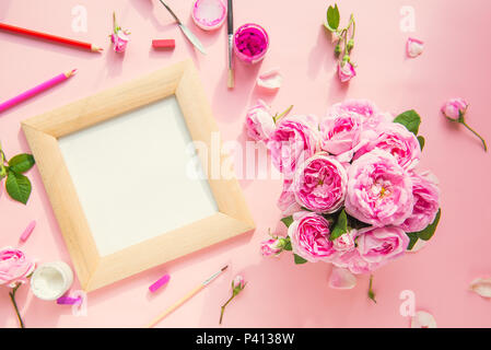 Top view canvas blank in wooden frame, art materials - colored pencils, brushes, gouache, pastel and pink tea roses bouquet on the pink background. Dr Stock Photo