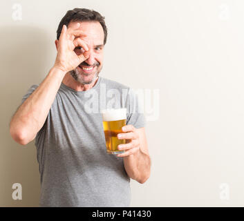 Senior man drinking beer with happy face smiling doing ok sign with hand on eye looking through fingers Stock Photo