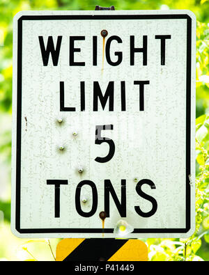 A weathered and cracked weight limit sign on a bridge over a wilderness stream in the Adirondack Mountains, NY USA with several bullet holes. Stock Photo